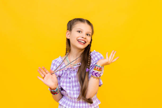 The child put on a lot of bracelets made of beads and beads. A happy little girl is enjoying a beaded ornament. Beading for children. Isolated yellow background.